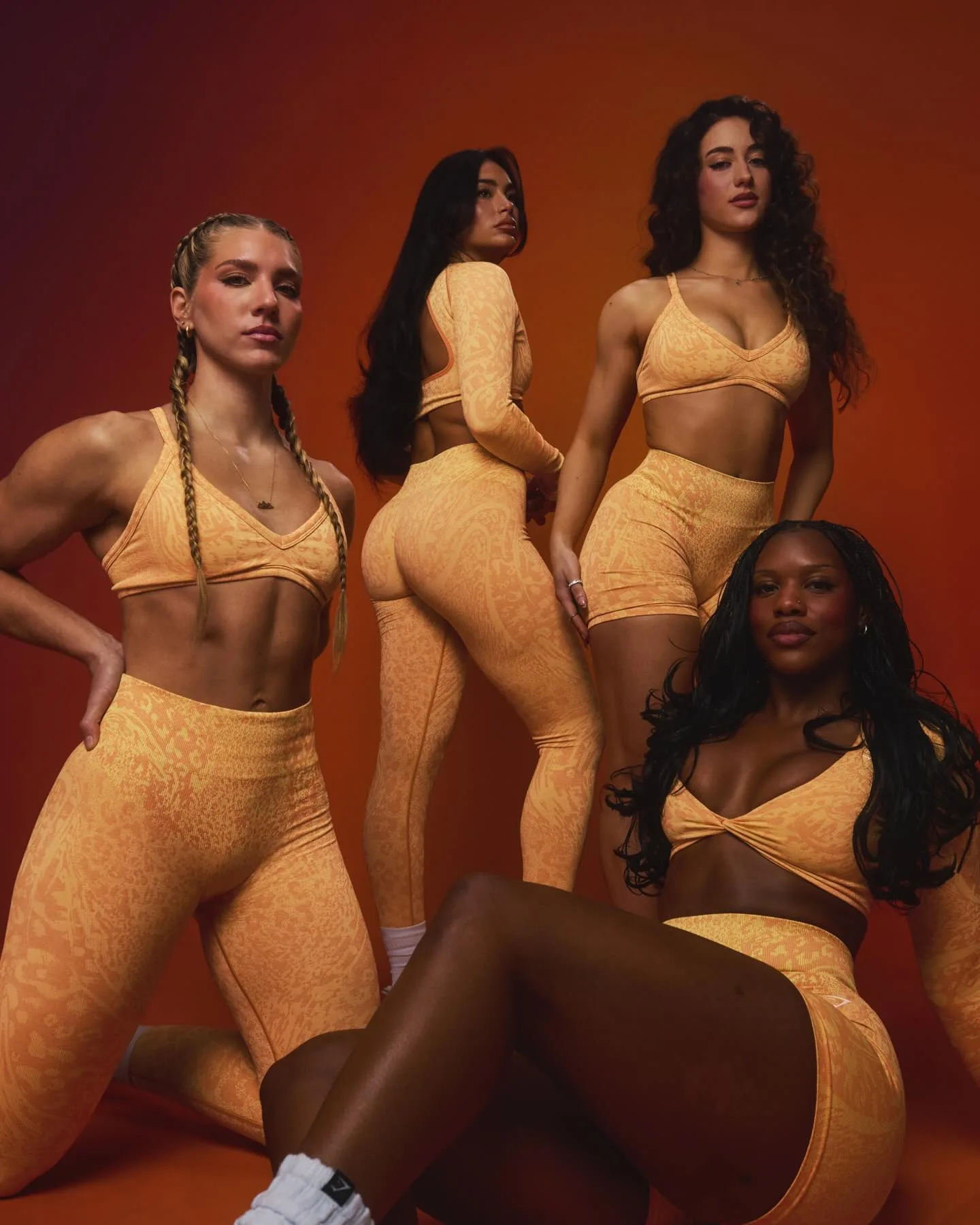 Four women athletes posing in the Gymshark Adapt Animal collection in "Sorbet Yellow," featuring animal-print seamless leggings, shorts and sports bras against a warm orange gradient background. For article: best activewear brands Australia