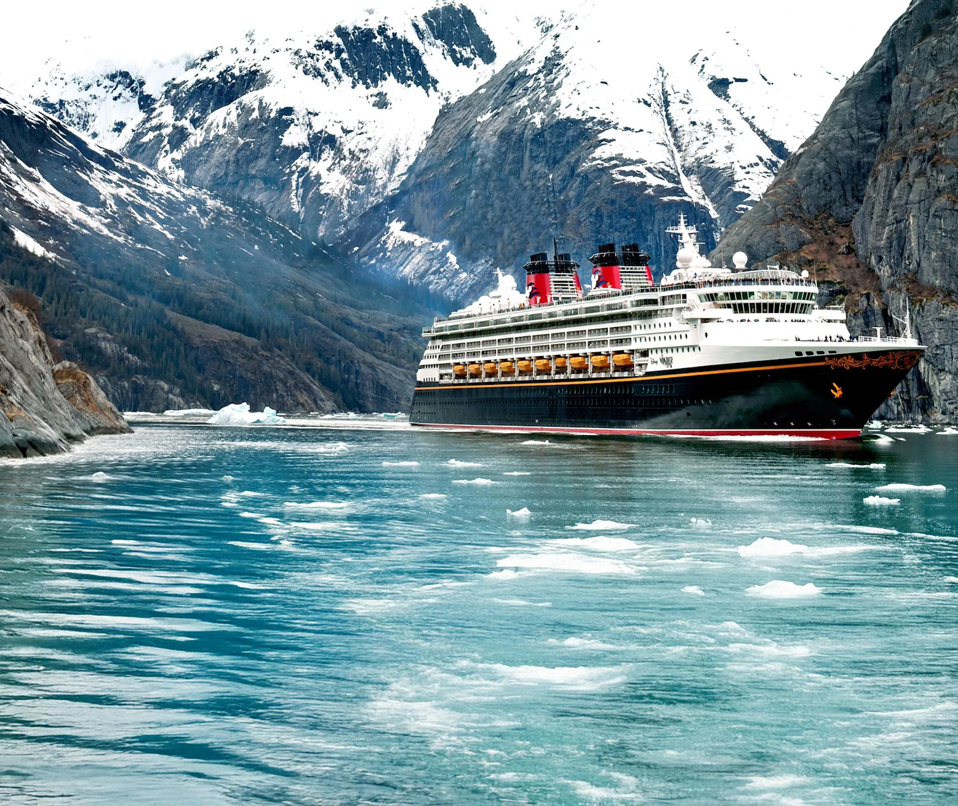 A cruise ship weaves through mountain scenery in Alaska.
