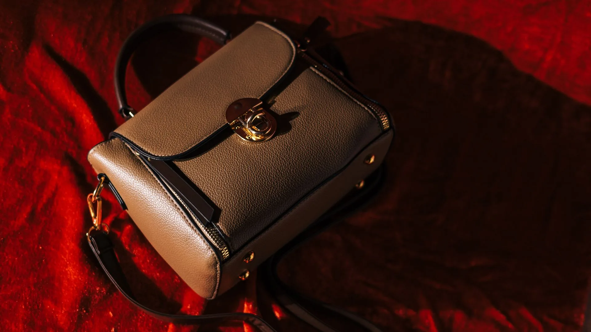 A structured taupe pebbled leather handbag with gold hardware on a red velvet background, showcasing classic styles for luxury handbags under $1000.