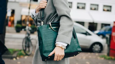 Close-up of a person in a grey coat holding a structured green croc-embossed tote, an example of the most durable designer bags.