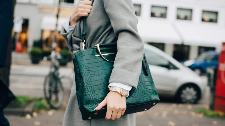 Close-up of a person in a grey coat holding a structured green croc-embossed tote, an example of the most durable designer bags.