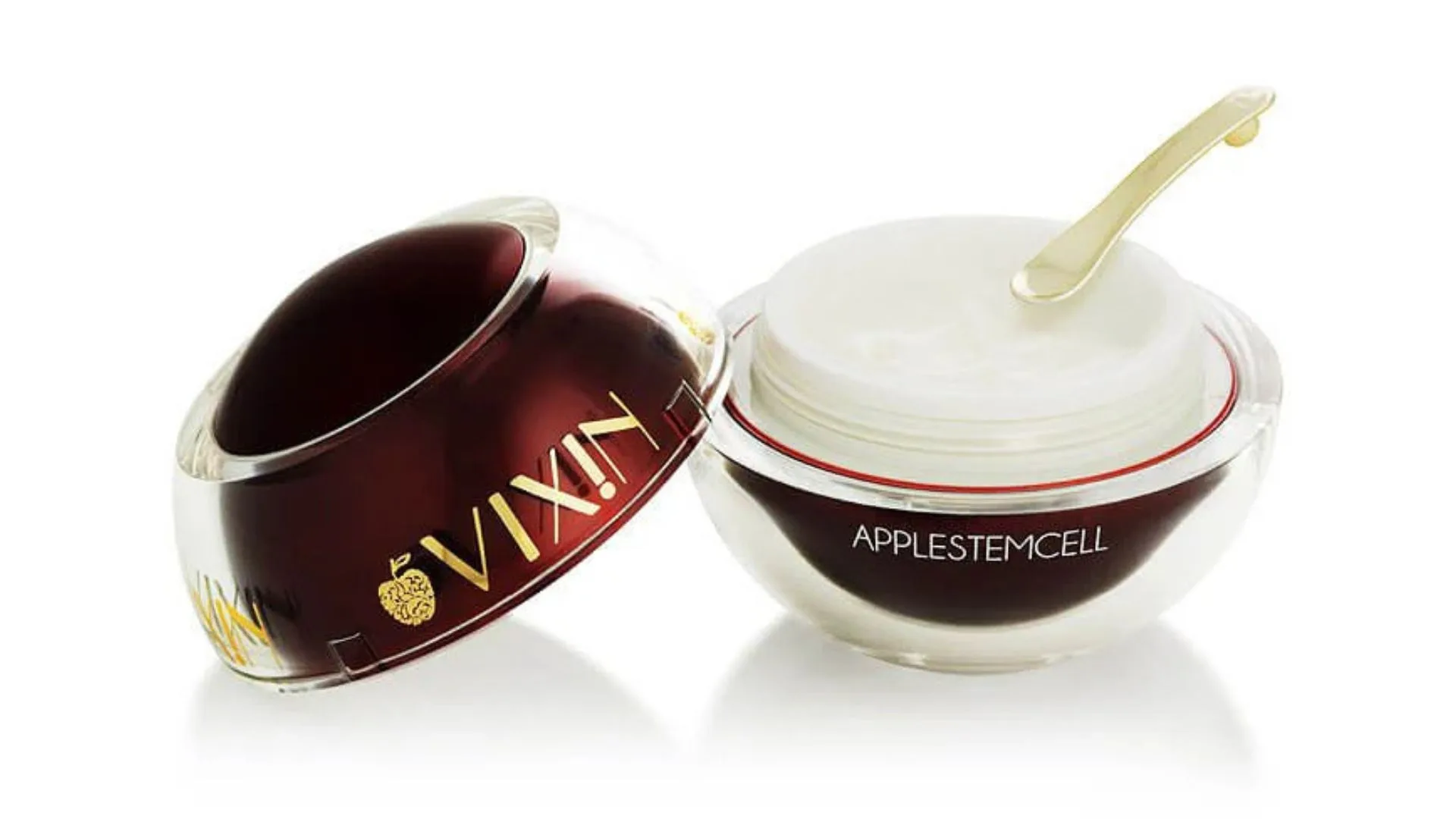 An open jar of Vixin Apple Stem Cell skincare cream with its round, deep red and clear lid resting beside it, showing the white cream inside and a small gold applicator spatula. Featured in the winter moisturiser for dry skin article.