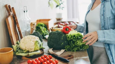 Woman unpacking fresh vegetables like broccoli, cauliflower, and capsicum on a kitchen benchtop for easy weeknight dinners.