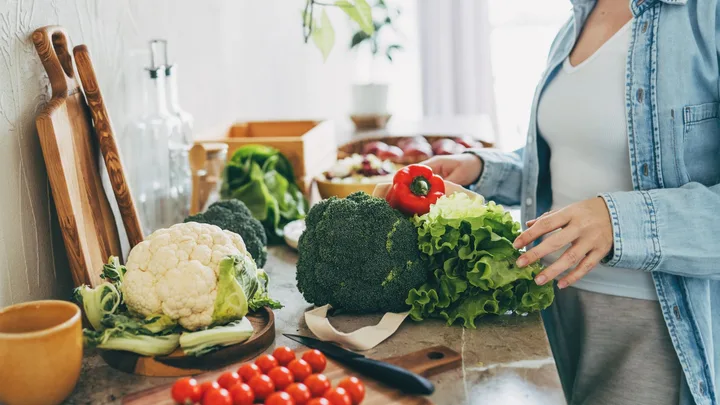 Woman unpacking fresh vegetables like broccoli, cauliflower, and capsicum on a kitchen benchtop for easy weeknight dinners.