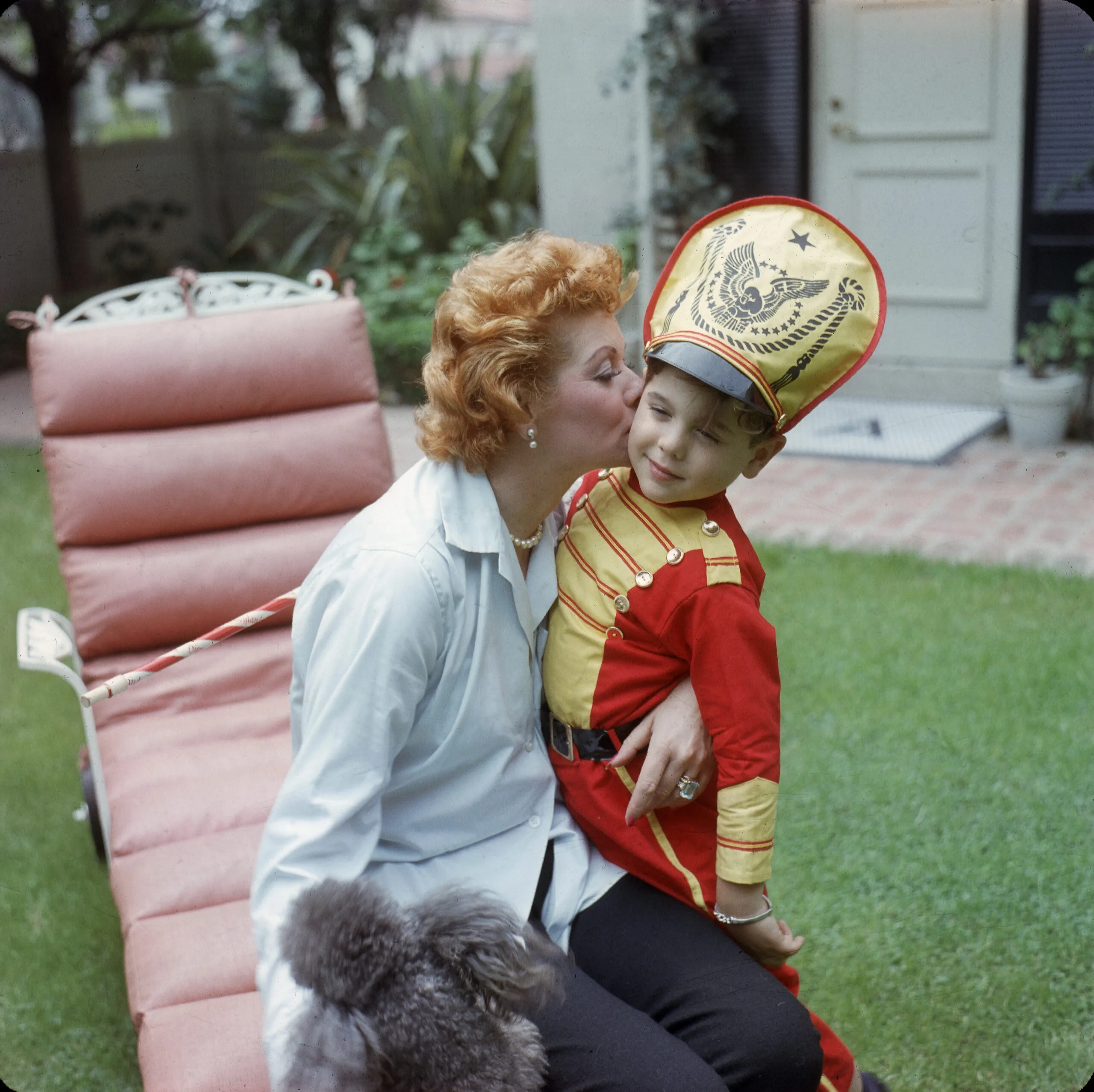 American actress and comedienne Lucille Ball (1911 - 1989) kisses her son Desi Arnaz Jr, who is dressed as a drum major with a baton, in the back yard of their home, Los Angeles, California, late 1950s. (Photo by Gene Lester/Getty Images)