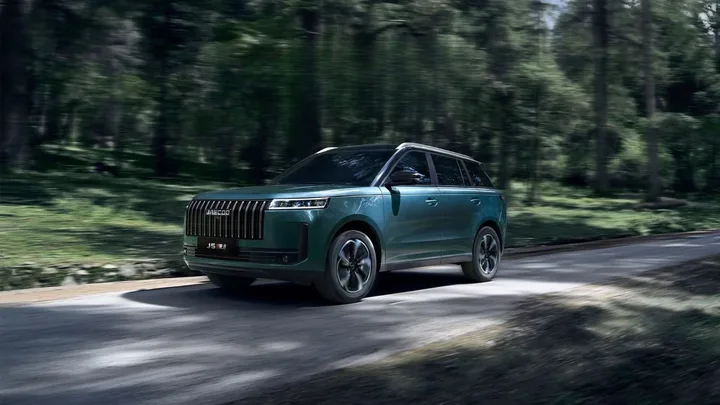 A dark green JAECOO hybrid SUV driving along a scenic tree-lined road in Australia.