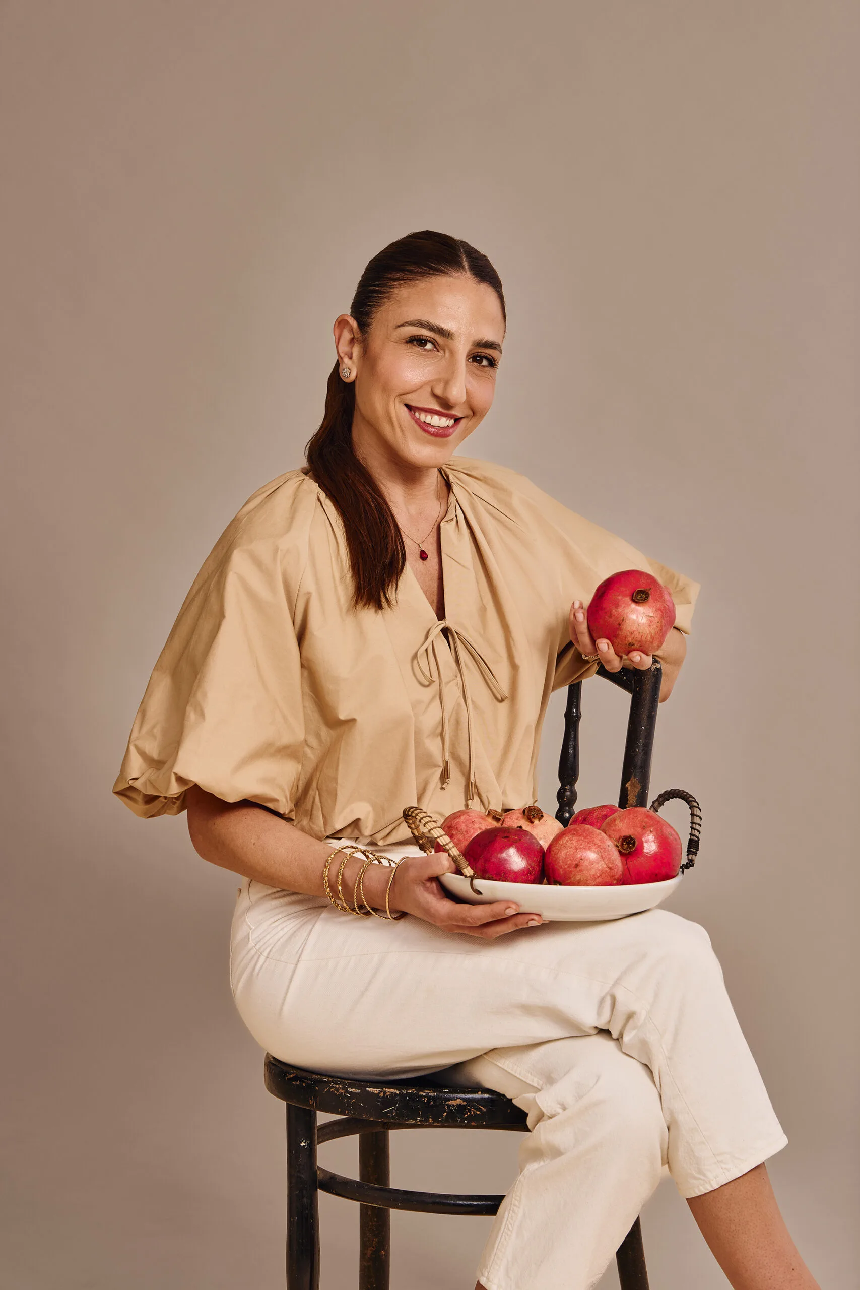 A woman sits on a chair holding a bowl of red fruits.