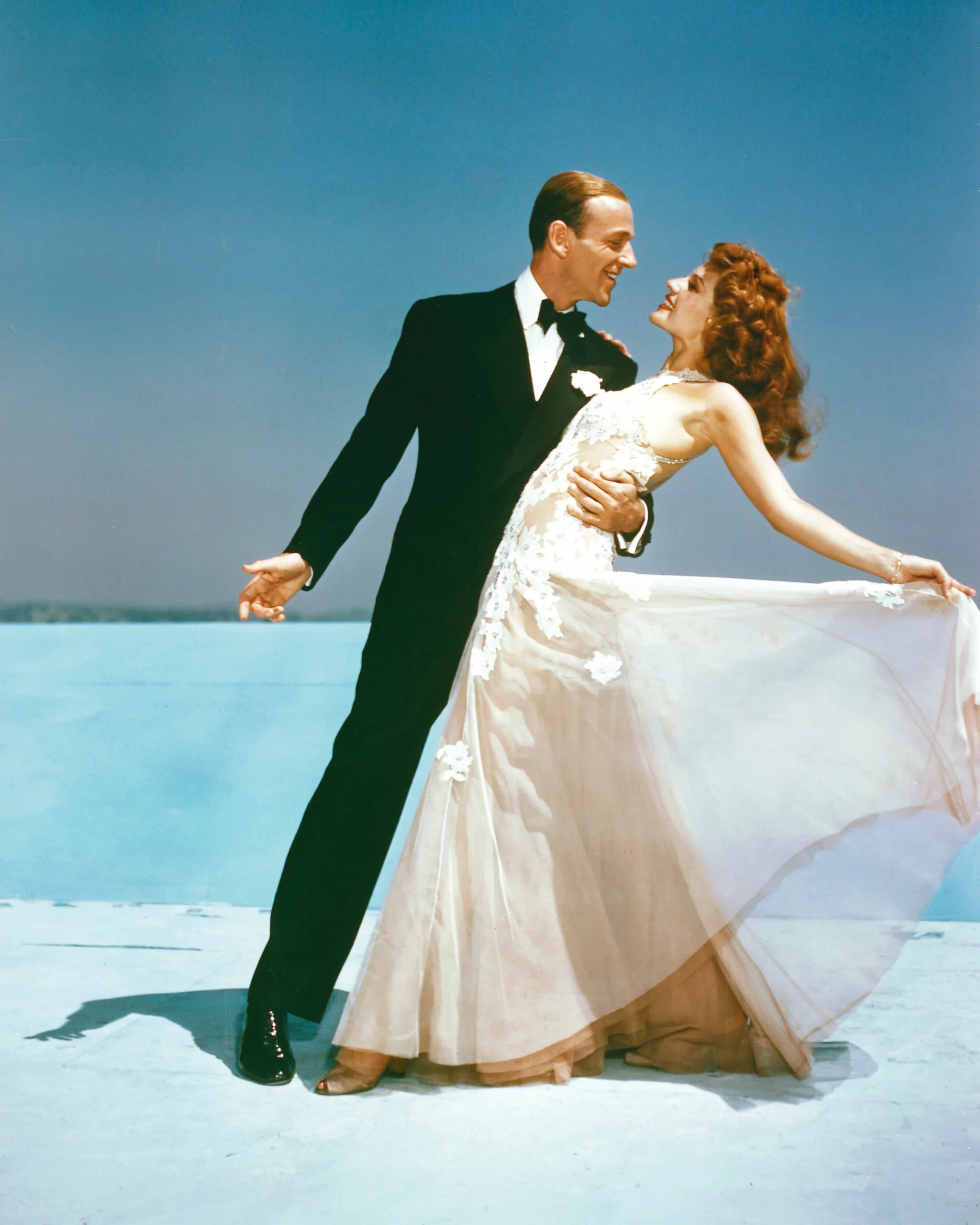 Fred Astaire (1899-1987), US actor and dancer, wearing a black dinner suit and bow tie, and Rita Hayworth (1921-2008), US actress and dancer, wearing a flowing white evening gown, holding a dance pose in studio portait, against a blue background in a publicity portrait issued for the film, 'You Were Never Lovelier', 1942. The musical, directed by William A. Seiter (1890-1964), starred Astaire as 'Robert 'Bob' Davis', and Hayworth as 'Maria Acuna'. (Photo by Silver Screen Collection/Getty Images)