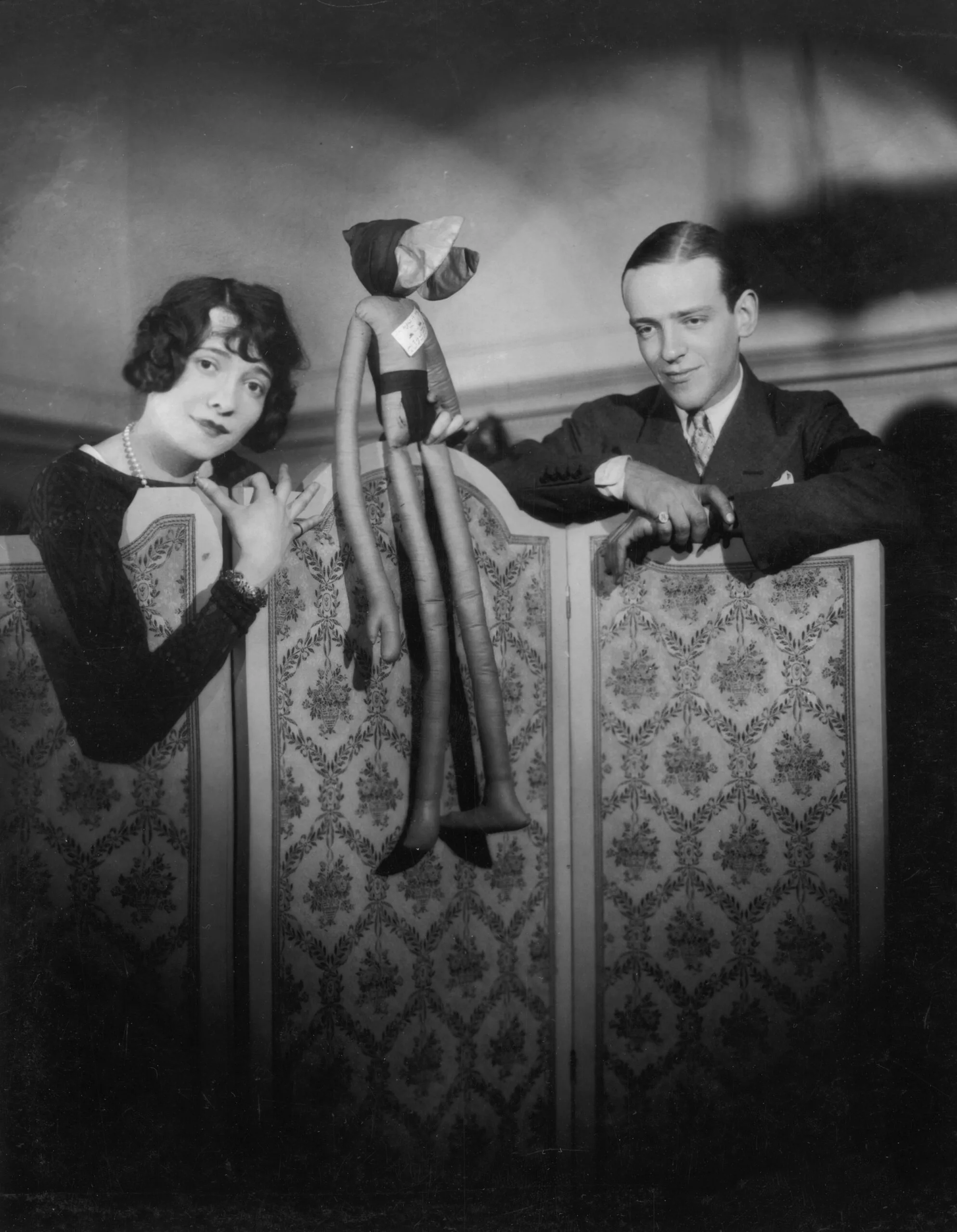 Hollywood dancer, singer and film actor Fred Astaire (1899 - 1987) and his sister Adele Astaire (1898 - 1981) standing behind a screen and holding a doll. (Photo by Sasha/Hulton Archive/Getty Images)