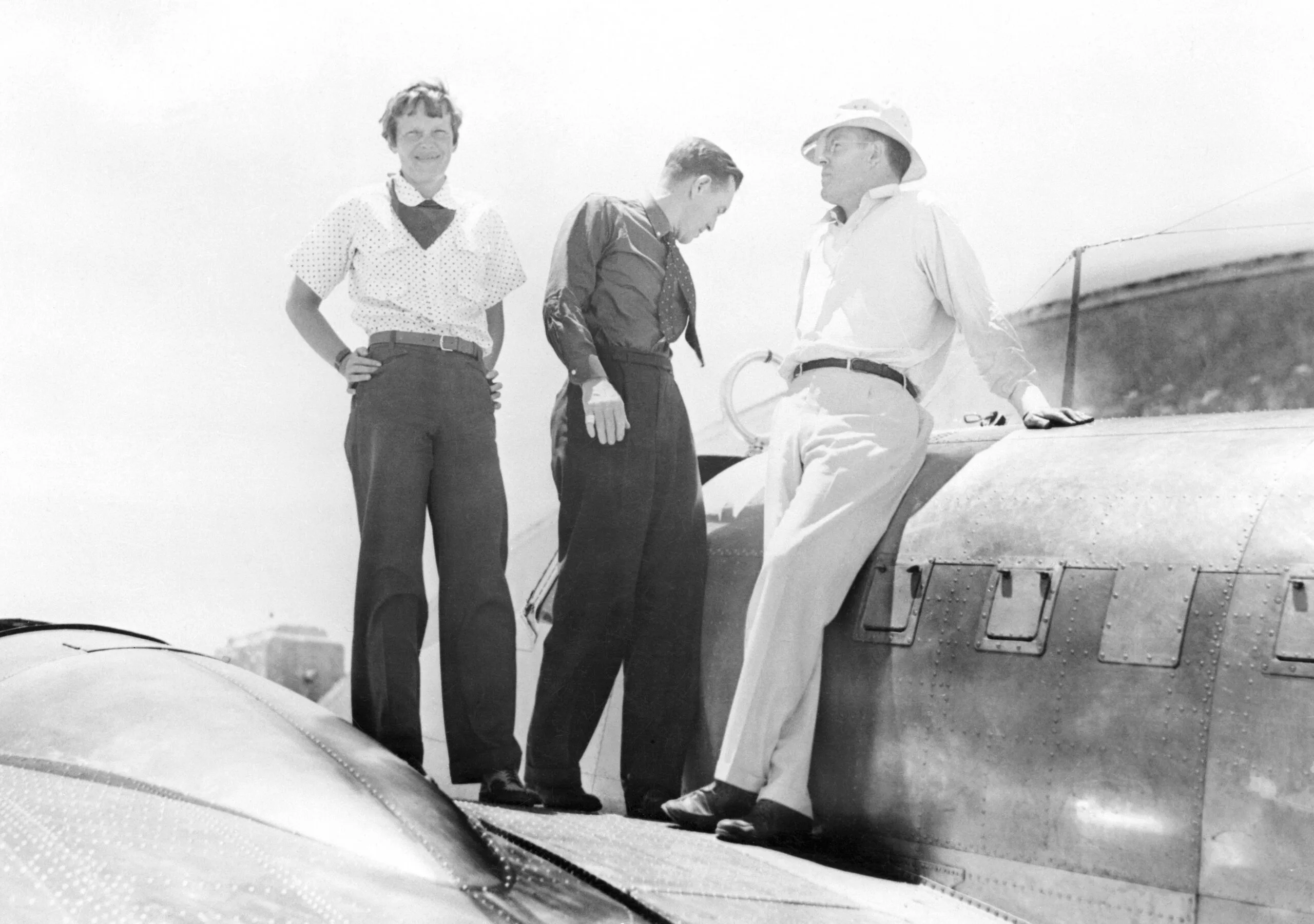 (Original Caption) Amelia Earhart Putnam discusses radio trouble on the wings of her plane, a twin motored monoplane (Lockheed), with Captain Fred Noonan, her navigator, (C), and her husband, George Palmery Putnam, (R), after a one hour and thirty minute test flight at Miami, May 30th, in preparation for a contemplated eastward world flight.