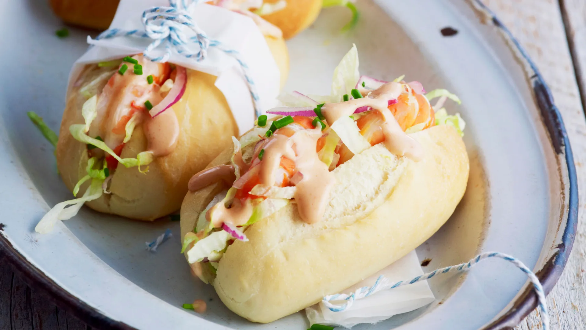 Two fresh prawn rolls on a plate drizzled with hot sauce.
