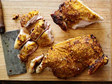 "Roasted chicken portions on a wooden board with a meat cleaver nearby."