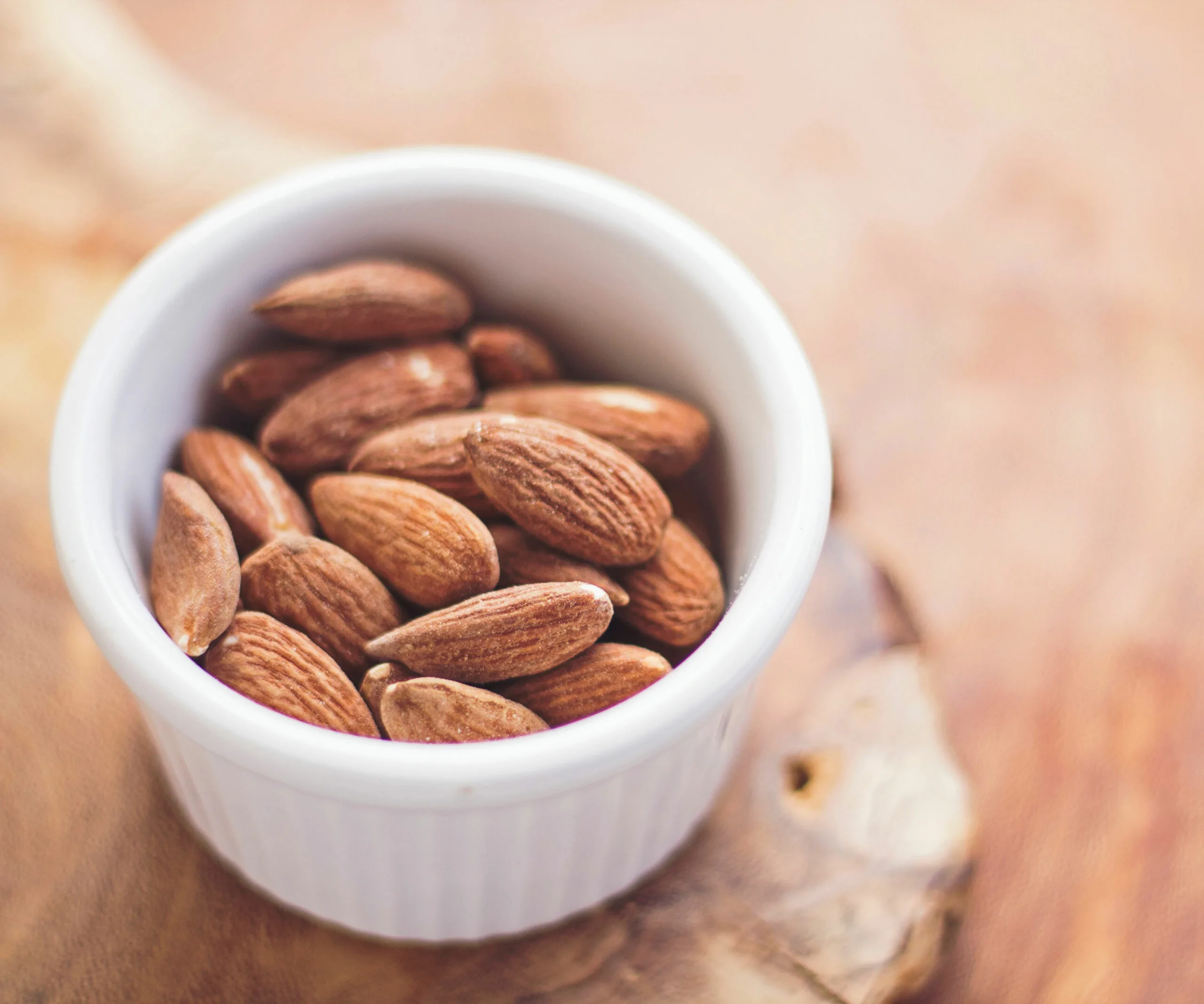 roasted and salted almonds in a white ramekin on a wooden table