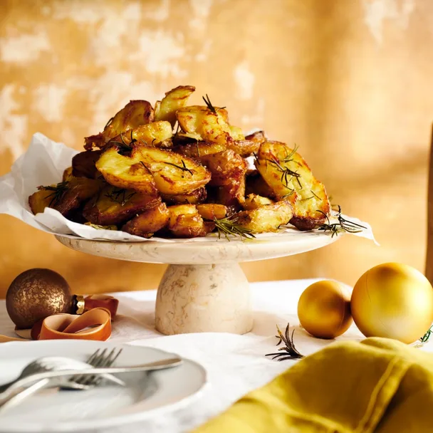 Maggie Beer's duck fat roast potatoes on a white display stand, with gold baubles around