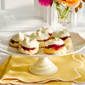 six gluten free scones on a white cake stand with jam and cream