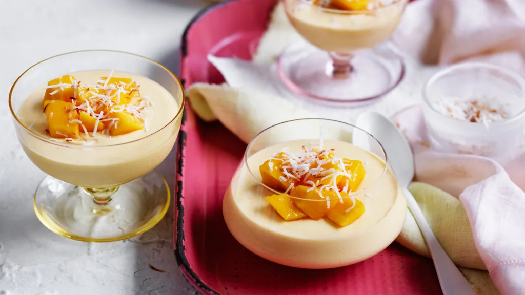 mango mousse in glass jars topped with mango pieces and coconut