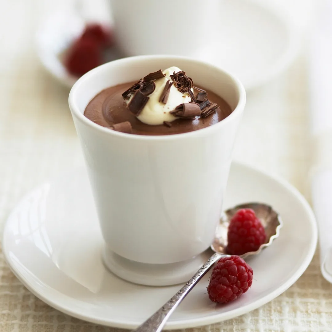chocolate mousse in a white dish topped with cream and chocolate curls