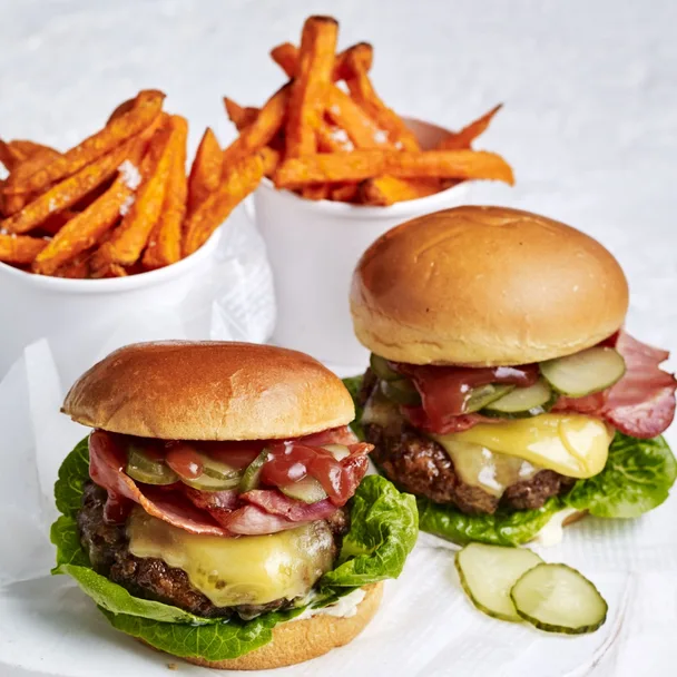 air fryer burger patties in two cheeseburgers with containers of sweet potato chips