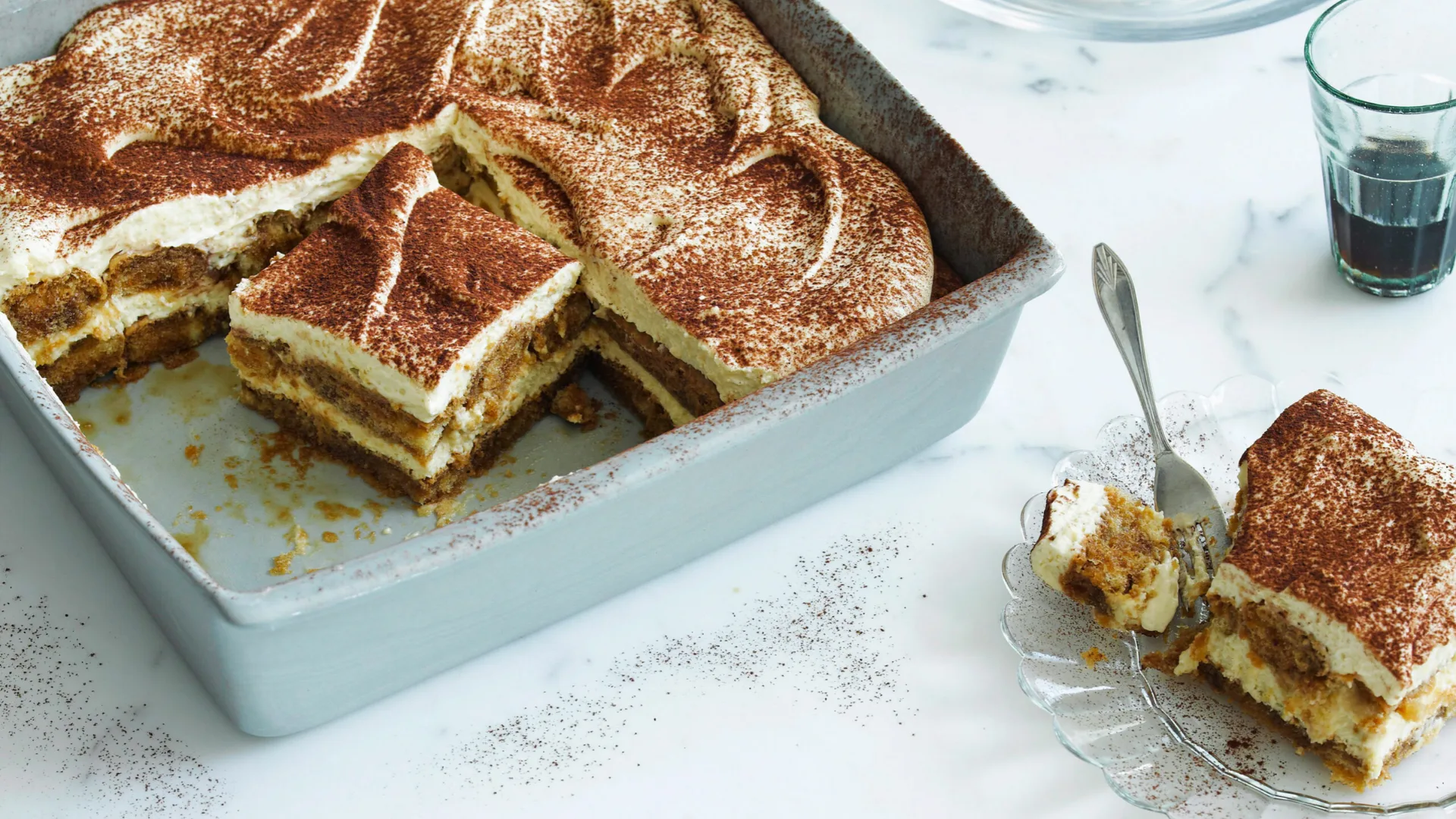 tiramisu cake in a tray, with a slice on a plate