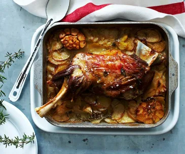 baked lamb shouder in a roasting tray with roast potatoes and garlic