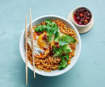 ramen noodles in a bowl, topped with greens and a fried egg