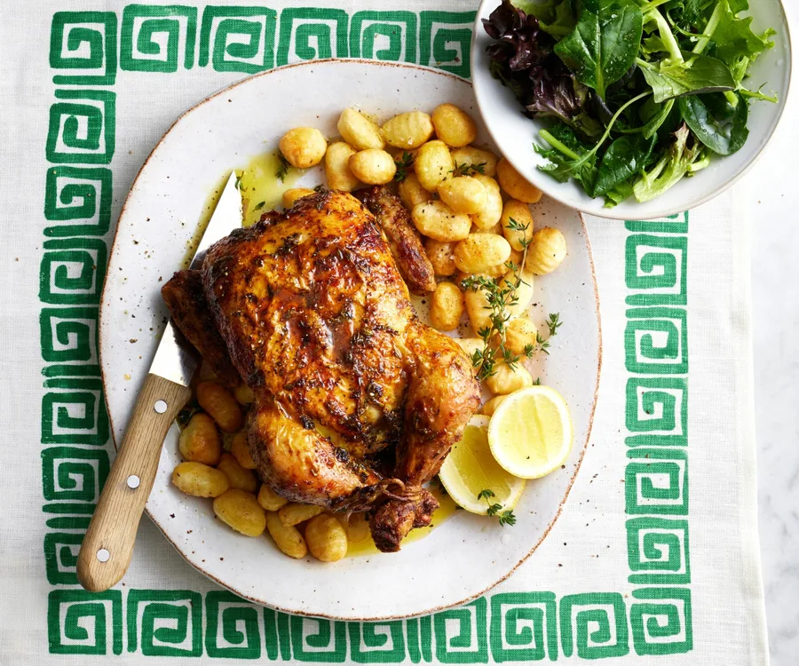 whole chicken on bed of potatoes on a plate