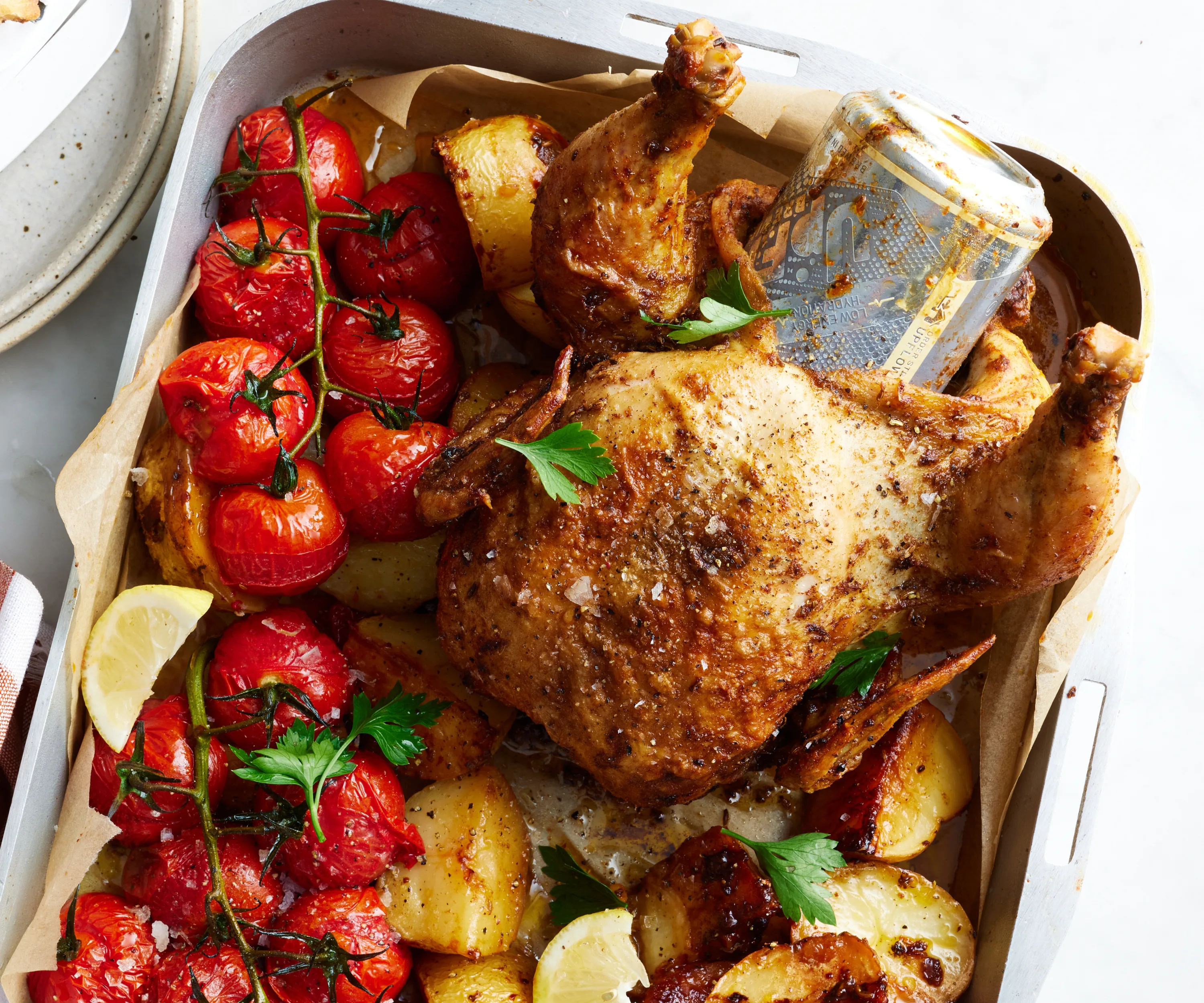Baking tray with beer can chicken, potatoes and tomatoes