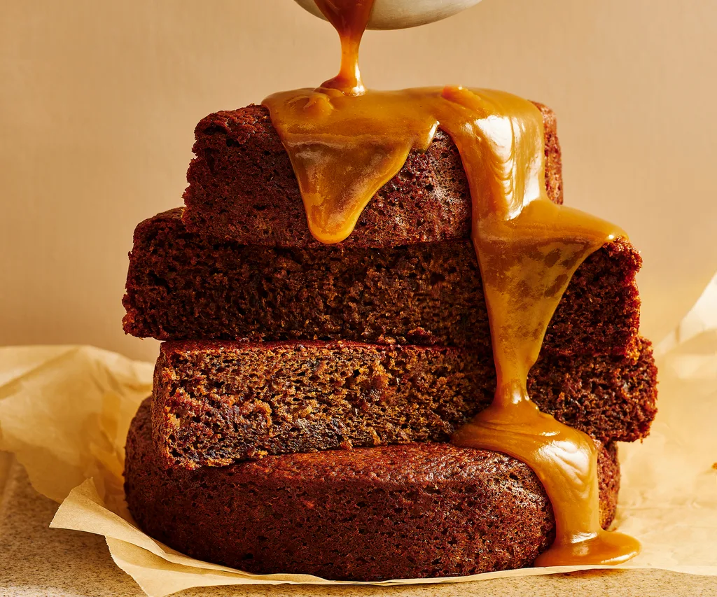 layers of sticky date pudding with sauce being poured over