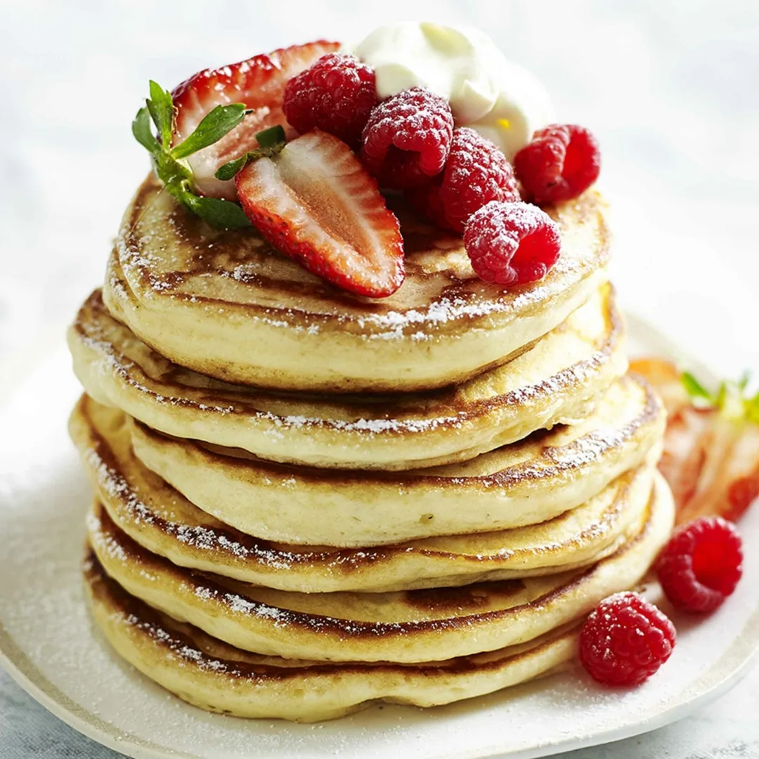 a stack of fluffy pancakes on a plate, topped with berries