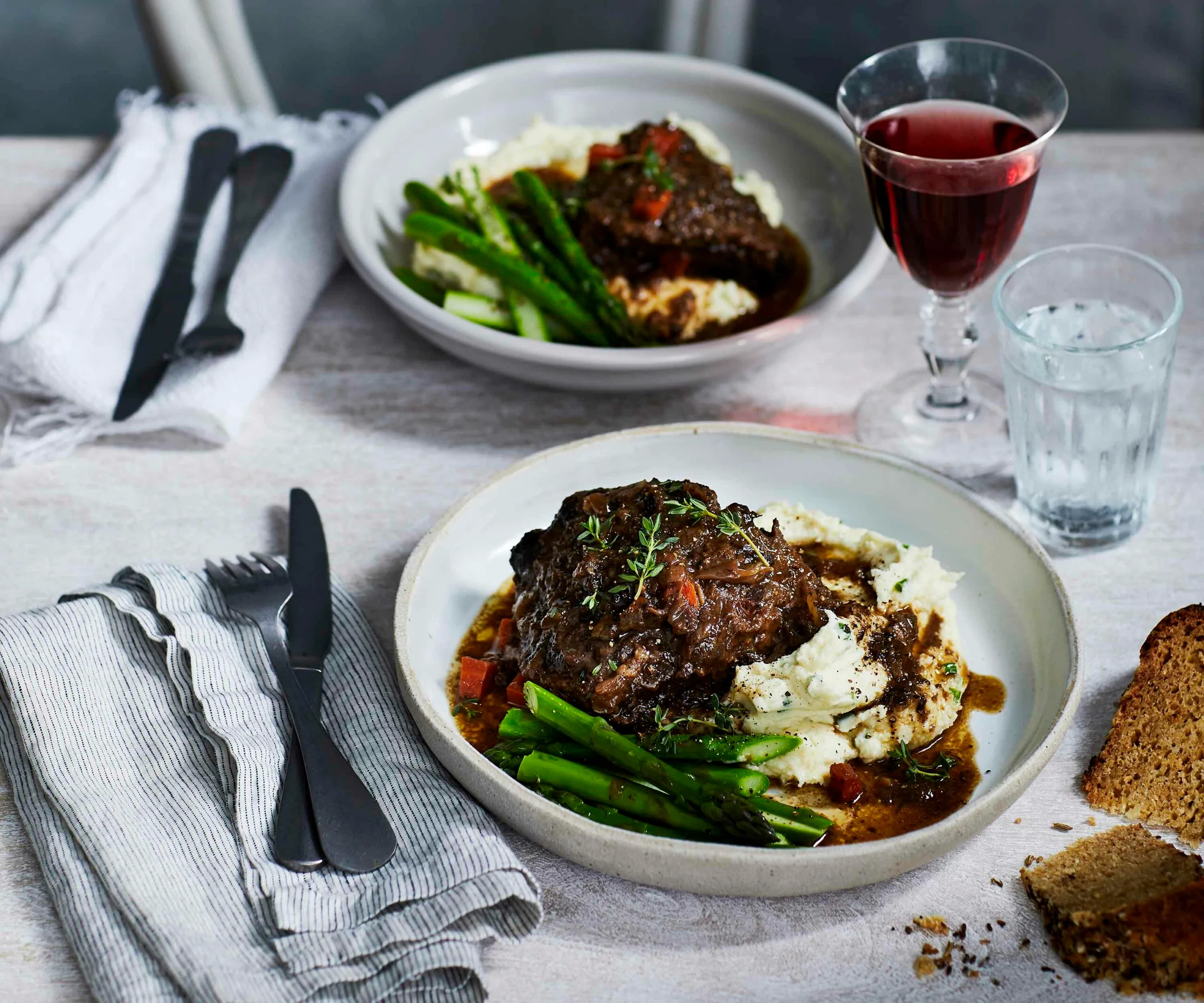 two bowls filled with beef cheeks, beans and mash on a set table