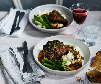 two bowls filled with beef cheeks, beans and mash on a set table