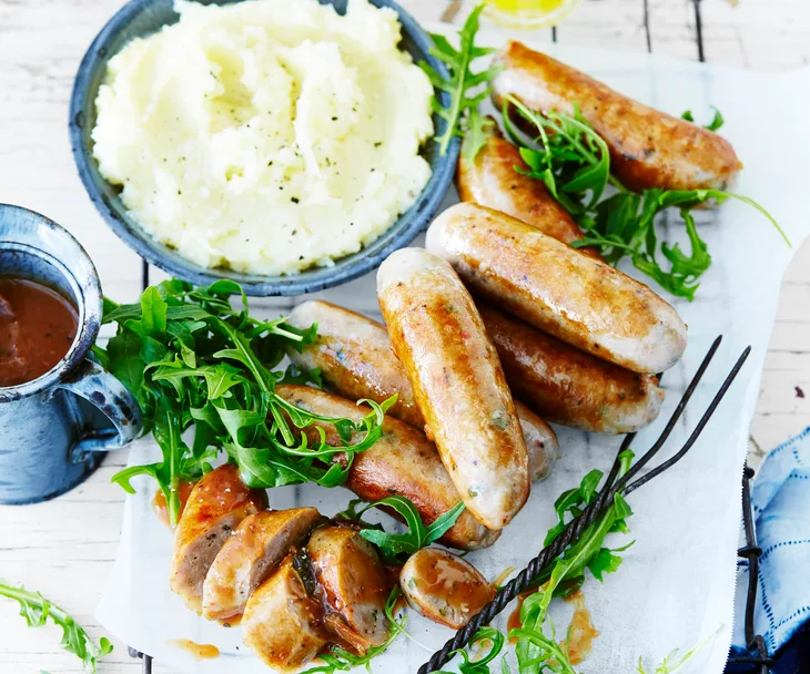 Plate of pork sausages, bowl of potato and parsnip mash, jug of gravy