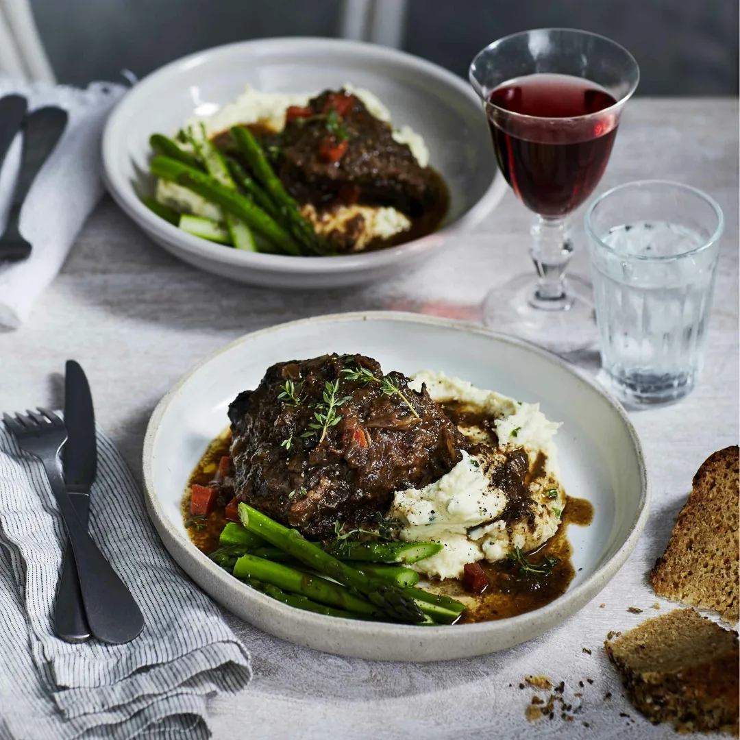 two bowls filled with slow cooker beef cheeks, beans and mash on a set table