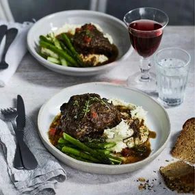 two bowls filled with slow cooker beef cheeks, beans and mash on a set table