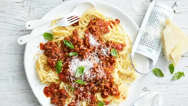 lentil and mince bolognese sauce on spaghetti on a white plate, topped with grated parmesan and basil for a freezer friendly meal