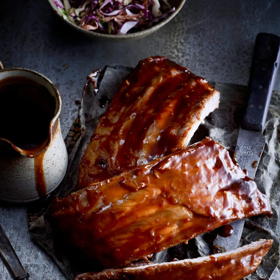 slow cooker pork ribs with sticky marinade in a jug and a bowl of cheesy coleslaw