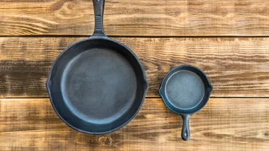 Two cast iron skillets, one large and one small, on a wooden surface.