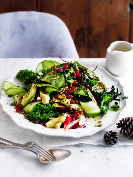 Green salad with red currants on serving platter with fork and spoon.