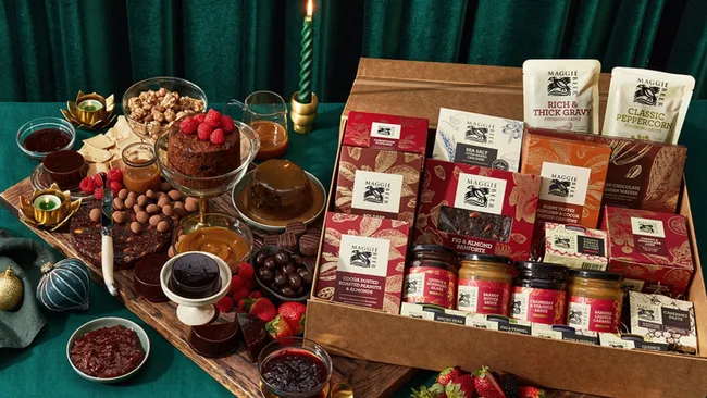 "Hamper with Maggie Beer products, chocolate, cake, and garnishes on a festive table with a green candle."