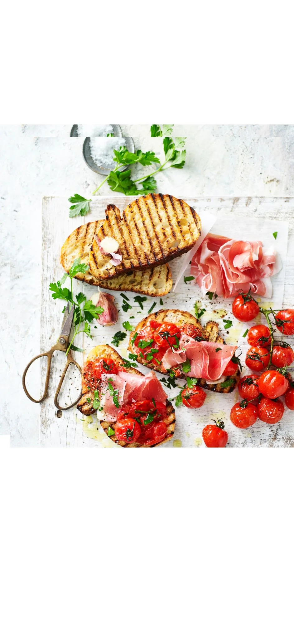 slices of grilled bread on chopping board topped with roasted truss tomatoes and jamon