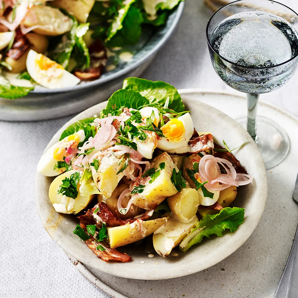 Spicy potato Caesar salad in a bowl and a glass of sparkling water