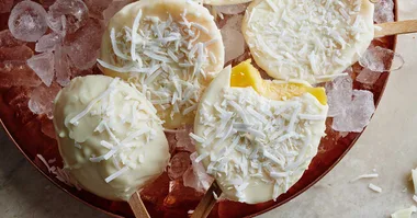 frozen mango covered in white chocolate on an ice cream stick