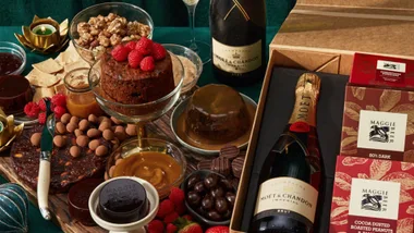 Luxury gift set with Moët & Chandon champagne, gourmet chocolates, nuts, and desserts on a green tablecloth.