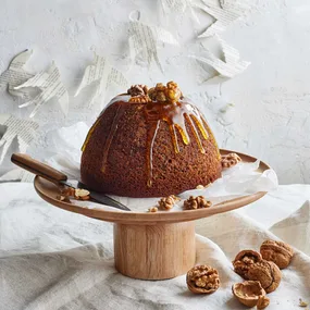 Whole sticky date pudding topped with toffee sauce and nuts on a cake stand
