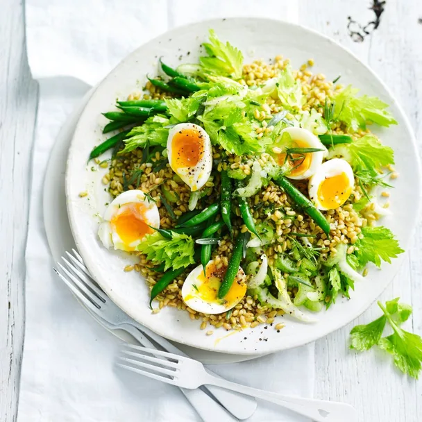 Salad of grain, green beans, celery and boiled eggs in a white serving bowl.