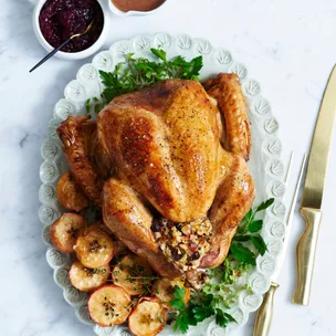 Whole roast turkey and stuffing on a white oval serving dish.