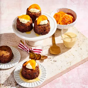 Mini Christmas puddings on a cake stand and plate with a jug of brandy sauce