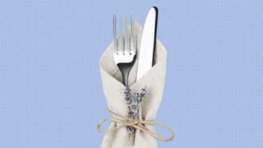 Napkin wrapped around fork and knife with lavender sprigs, tied with twine, against a light blue dotted background.