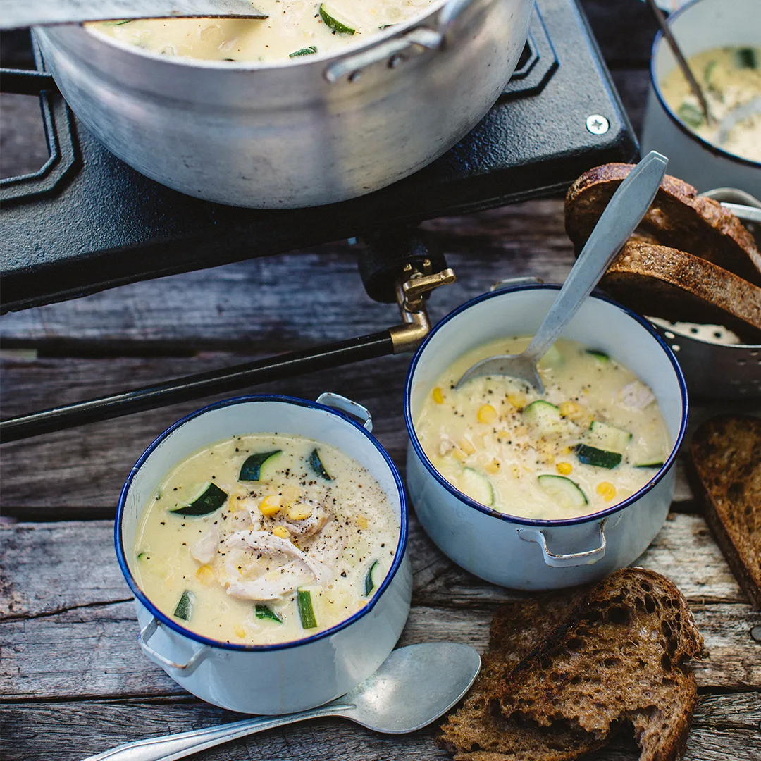 Two bowls of creamed corn, zucchini & chicken soup in front of a pot of soup