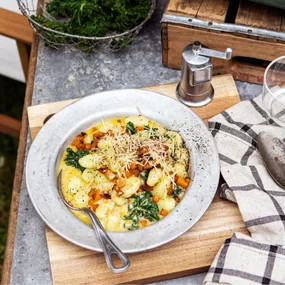 Creamy gnocchi with kale, walnuts, and cheese on a wooden table with a pepper mill and kitchen towel.